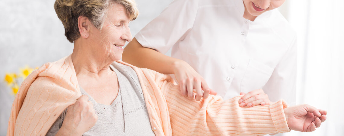 Betreuerin hilft einer älteren Frau nach Schlaganfall beim Anziehen